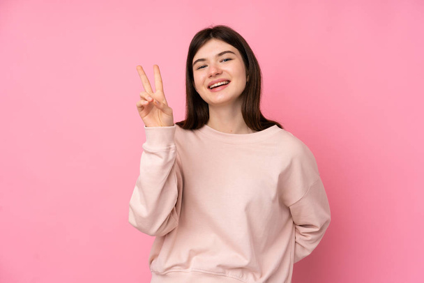 Молода українська дівчинка - підліток через ізольований рожевий фон посміхається і показує знак перемоги - Фото, зображення