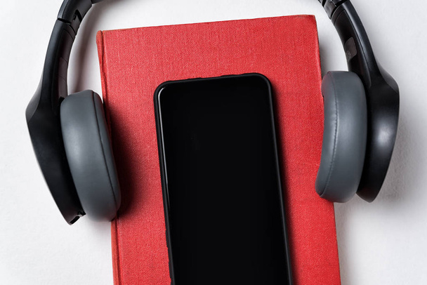 Ακουστικά, βιβλίο και κινητό τηλέφωνο σε λευκό φόντο. Βιβλίο ή audiobook έννοια. Αντιγραφή χώρου, κοντινό - Φωτογραφία, εικόνα