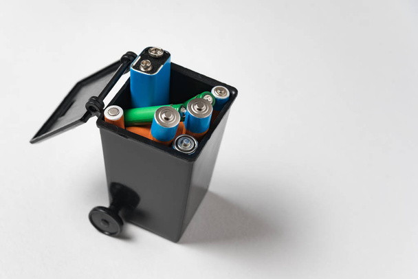 Batteries in garbage container on white background. Battery recycling concept. Environmental pollution with toxic household waste. - Photo, Image