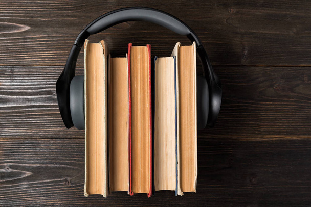 Ακουστικά που φοριούνται σε μια στοίβα από παλιά βιβλία σε ξύλινο φόντο. Αγαπημένο ηχητικό βιβλίο. Άνω όψη - Φωτογραφία, εικόνα
