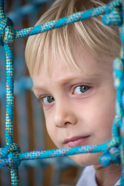 A kisfiú figyelmesen néz a kamerába. A gyerek átlát a hálón. Portré függőleges keret - Fotó, kép