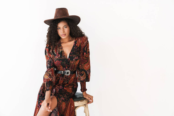 Image of african american cowgirl in dress and hat sitting on ch - Фото, изображение
