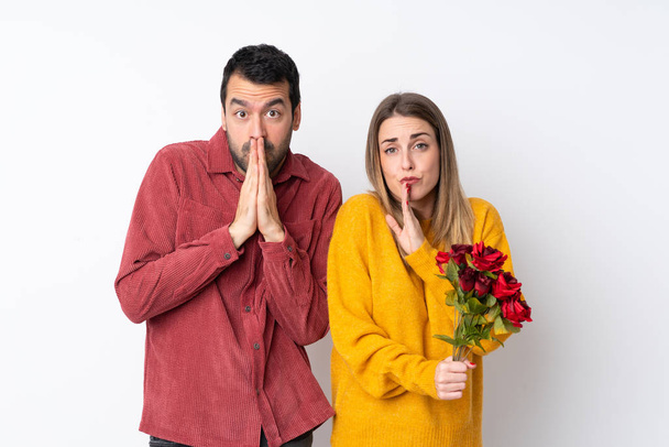 Couple in Valentine Day holding flowers over isolated background keeps palm together. Person asks for something - Photo, Image