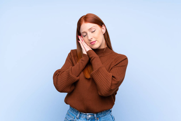 Young redhead woman over isolated blue background making sleep gesture in dorable expression - Fotoğraf, Görsel