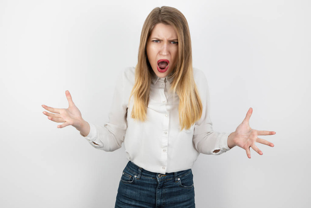 young beatuiful blond angry woman looks furious standing on isolated white background, splash of emotions - Photo, Image