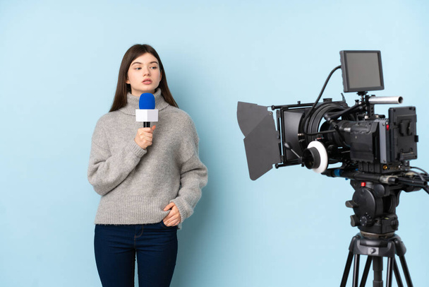 Reportérka drží mikrofon a hlásí zprávy na izolovaném modrém pozadí - Fotografie, Obrázek