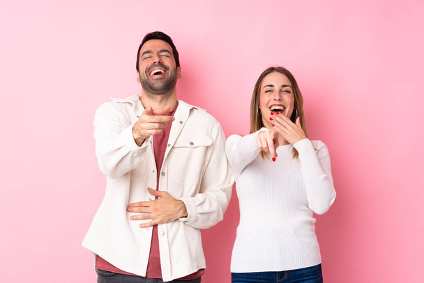 Пара в День святого Валентина над ізольованим рожевим фоном вказує пальцем на когось і багато сміється - Фото, зображення