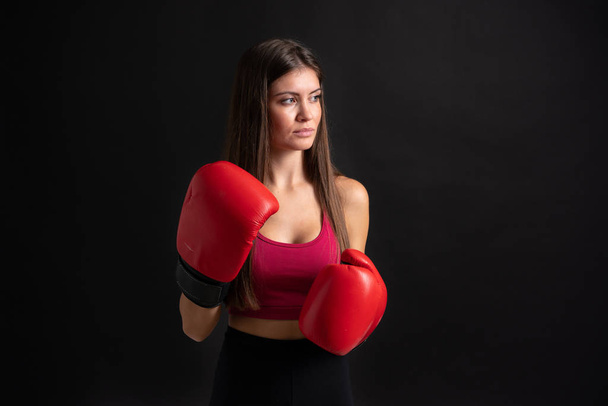 Νεαρή αθλητική γυναίκα με γάντια πυγμαχίας πάνω από απομονωμένο μαύρο φόντο - Φωτογραφία, εικόνα