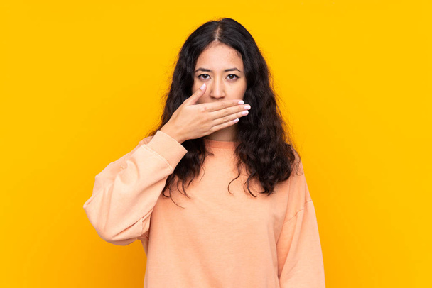 Spaanse Chinese vrouw over geïsoleerde gele achtergrond bedekken mond met handen - Foto, afbeelding