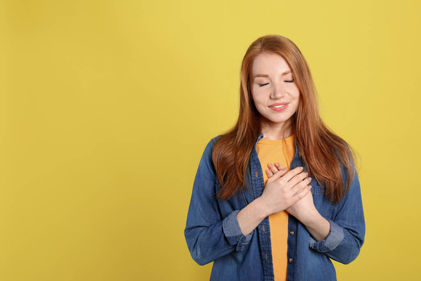Beautiful grateful woman with hands on chest against yellow back - Foto, imagen