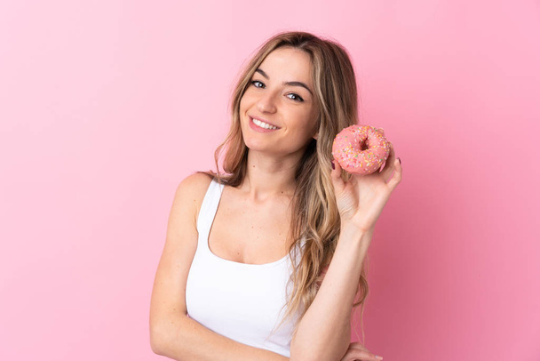 Young woman over isolated pink background holding a donut and happy - Photo, Image