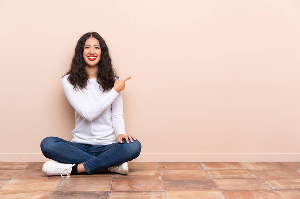 Young woman sitting on the floor pointing back - Photo, Image