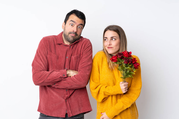 Couple dans la Saint-Valentin tenant des fleurs sur fond isolé faire des doutes geste tout en soulevant les épaules
 - Photo, image