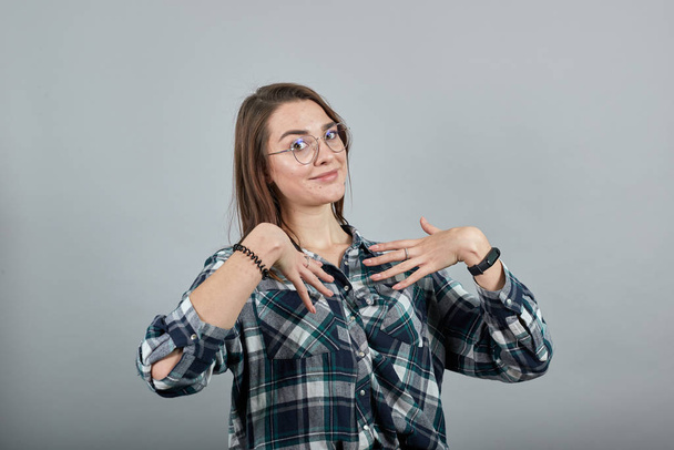 on grey background confident woman in glasses shows hands on herself - 写真・画像