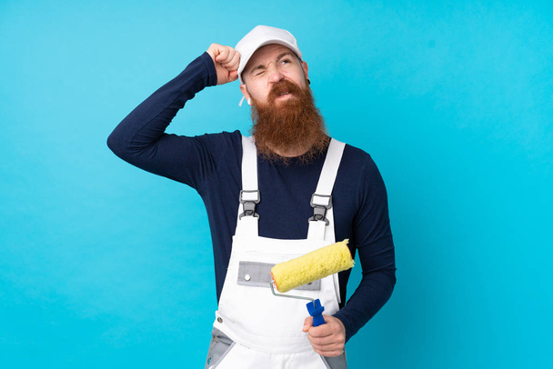 Homem pintor com barba longa sobre fundo azul isolado com dúvidas e com expressão facial confusa - Foto, Imagem