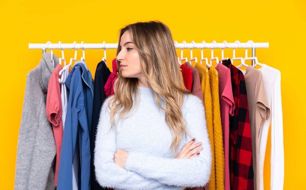 Young woman in a clothing store over isolated yellow background looking side - Photo, Image