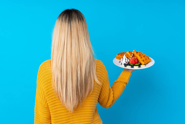 Jovem mulher segurando waffles sobre fundo isolado na posição traseira
 - Foto, Imagem