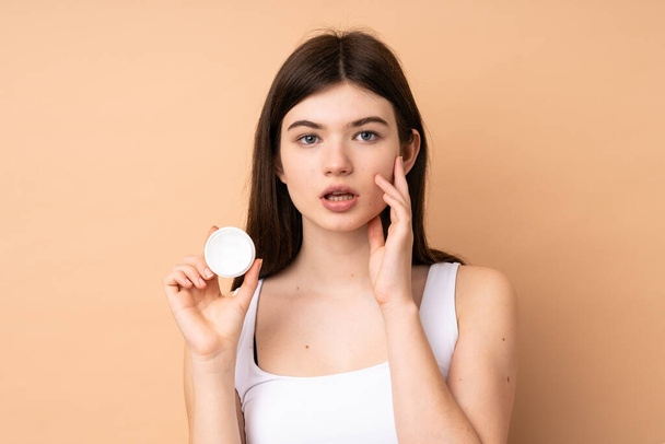 Young Ukrainian teenager girl over isolated background with moisturizer - Zdjęcie, obraz