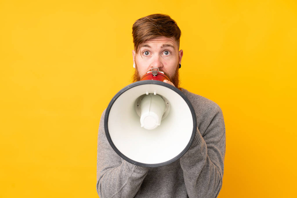 Redhead man with long beard over isolated yellow background shouting through a megaphone - Foto, immagini