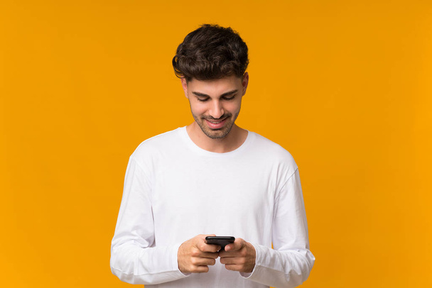 孤立したオレンジの背景の上に若い男は携帯電話でメッセージを送信 - 写真・画像