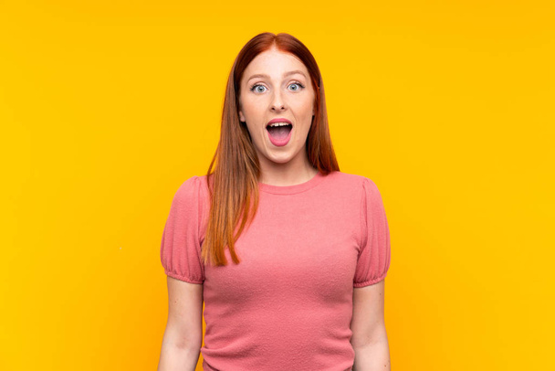 Jonge roodharige vrouw over geïsoleerde gele achtergrond met verrassing gezichtsuitdrukking - Foto, afbeelding