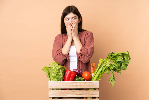 Молодая фермерская девушка со свежесобранными овощами в коробке нервничает и боится положить руки в рот
 - Фото, изображение