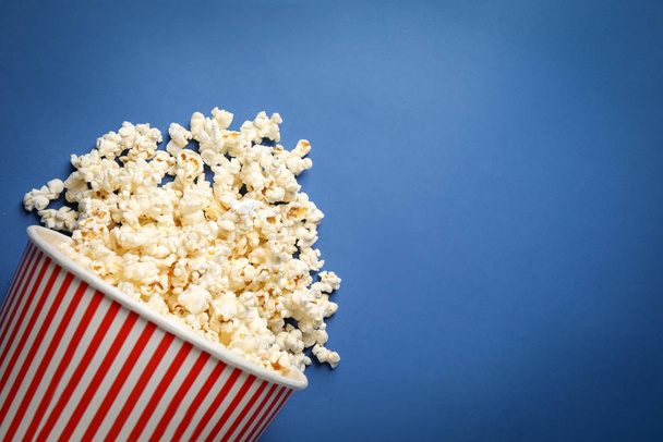 Overturned paper bucket with delicious popcorn on blue background, top view. Space for text - 写真・画像
