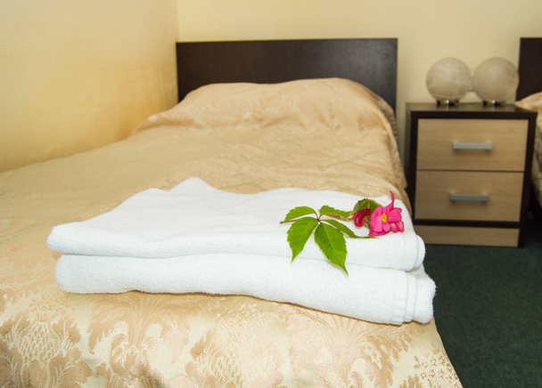 Innenraum des Hotels mit einem Bett mit einer luxuriösen goldenen Bettdecke und einem Satz weißer Handtücher mit einer Blume - Foto, Bild