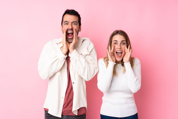 Couple in Valentine Day over isolated pink background shouting and announcing something - Photo, Image