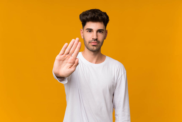 Junger Mann vor orangefarbenem Hintergrund macht Stop-Geste - Foto, Bild