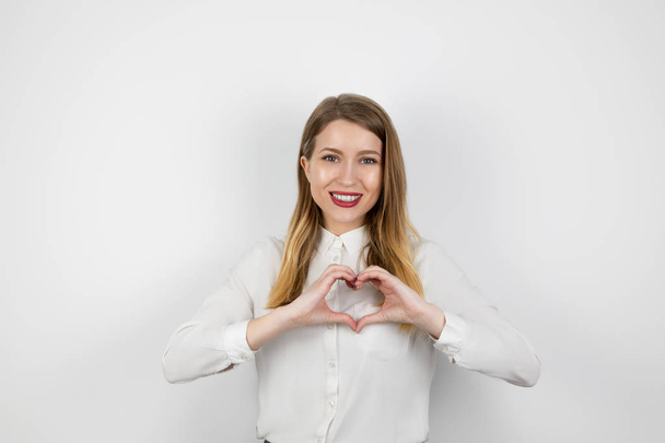 young blond woman making heart symbol with her hands standing on isolated white background, body language, lovely - 写真・画像