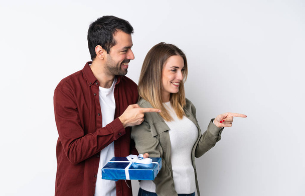 Couple in Valentine Day holding a gift over isolated background pointing finger to the side - Фото, зображення