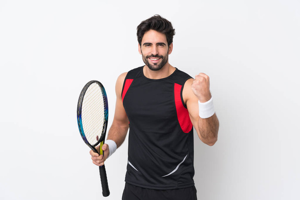 Young handsome man with beard over isolated white background playing tennis and celebrating a victory - Photo, Image