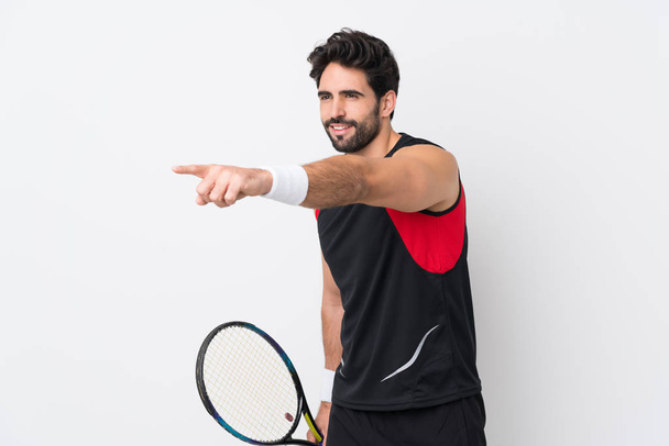 Jeune homme beau avec barbe sur fond blanc isolé jouant au tennis - Photo, image