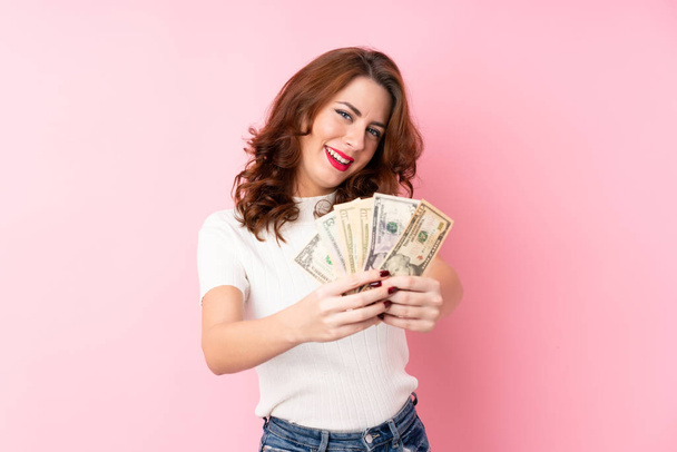 Jovem mulher russa sobre isolado fundo rosa tendo um monte de dinheiro
 - Foto, Imagem