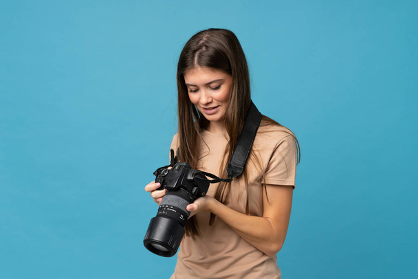 junge Frau vor isoliertem blauen Hintergrund mit einer professionellen Kamera - Foto, Bild
