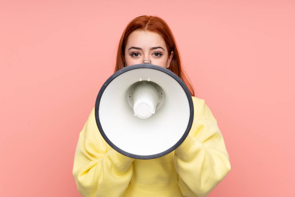 Redhead teenager girl over isolated pink background shouting through a megaphone - Фото, изображение