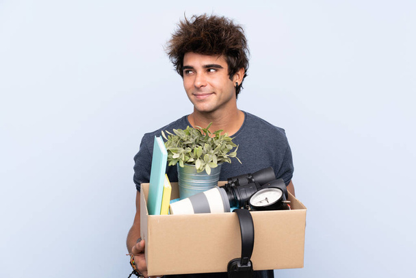 Man maakt een beweging tijdens het oppakken van een doos vol met dingen staan en kijken naar de zijkant - Foto, afbeelding