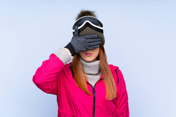 Skier rousse femme avec des lunettes de snowboard sur le mur bleu isolé couvrant les yeux par les mains
 - Photo, image