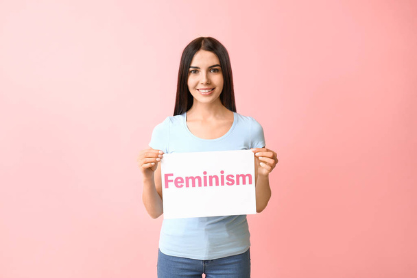 Young woman holding paper with text FEMINISM on color background - Фото, изображение