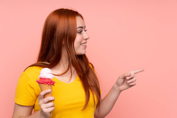 Mladá dívka s kornetovou zmrzlinou přes izolované pozadí ukazuje do strany prezentovat produkt - Fotografie, Obrázek