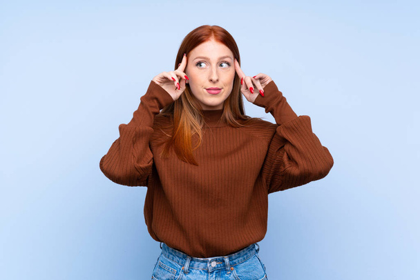 Fiatal vörös hajú nő izolált kék háttér, amelynek kétségei és gondolkodás - Fotó, kép