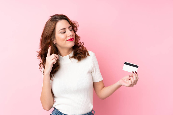 Jovem mulher russa sobre fundo rosa isolado segurando um cartão de crédito
 - Foto, Imagem