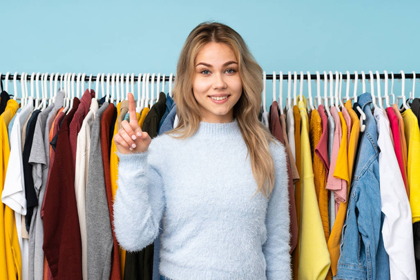 Teenager Russian girl buying some clothes isolated on blue background showing and lifting a finger in sign of the best - Fotoğraf, Görsel