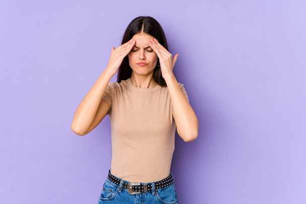Young caucasian woman isolated on purple background having a head ache, touching front of the face. - Photo, image
