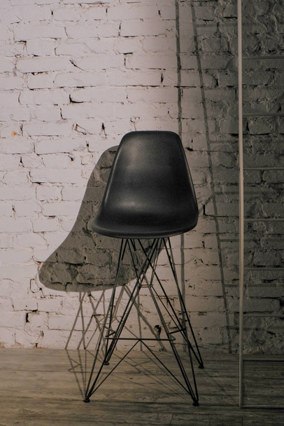 Black bar stool on a metal platoon carcass against a white brick wall - Foto, imagen