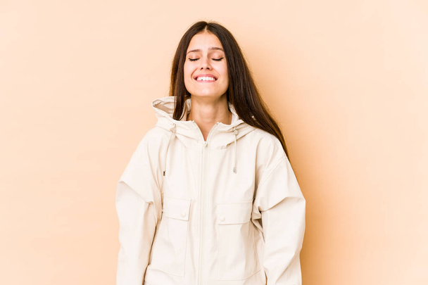 jonge blanke vrouw geïsoleerd op beige achtergrond lacht en sluit ogen, voelt zich ontspannen en gelukkig. - Foto, afbeelding