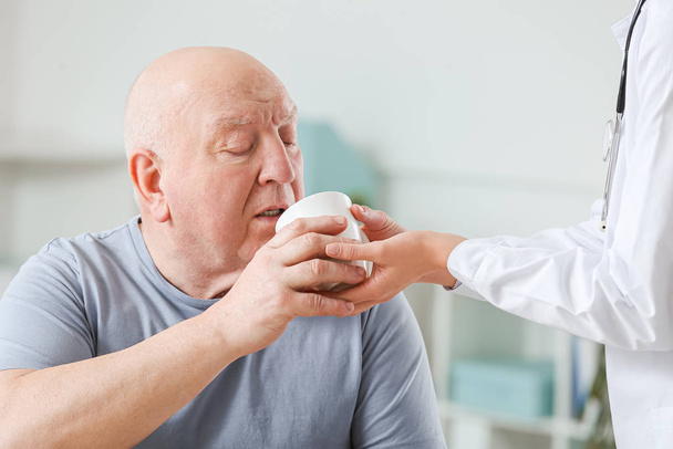Female doctor giving senior man suffering from Parkinson syndrome cup of tea in clinic - Photo, Image