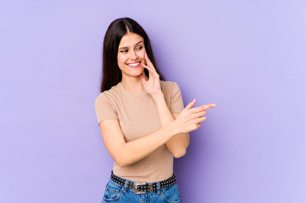Young caucasian woman isolated on purple background saying a gossip, pointing to side reporting something. - Photo, Image