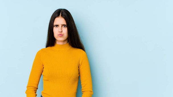 Young caucasian woman isolated on blue background blows cheeks, has tired expression. Facial expression concept. - Foto, Imagen